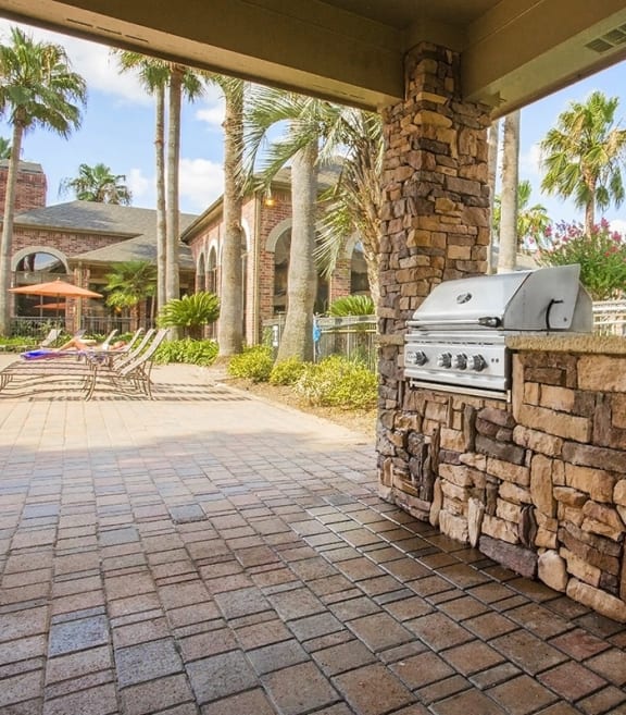 a barbecue grill on a stone wall in a patio with palm trees