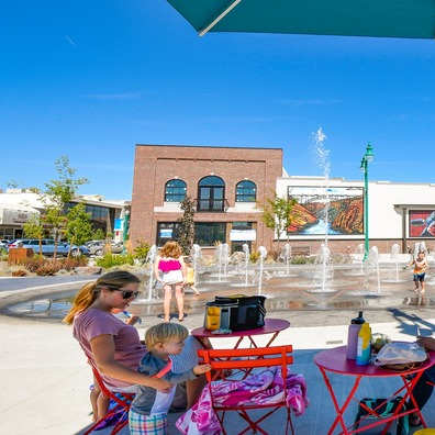 A family is sitting at a table under a green umbrella in a sunny outdoor seating area.