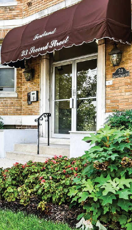 the front of a brick building with an awning and a flower garden