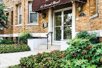 the front of a brick building with an awning and a flower garden