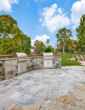 a patio with a stone wall and a grill in front of a house