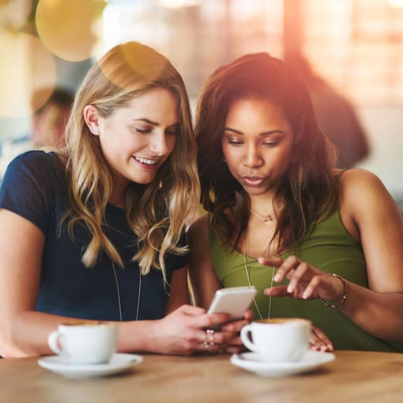 two women sitting at a table in a restaurant looking at a cell phone at Stone Creek at Old Farm Apartments, Houston, Texas