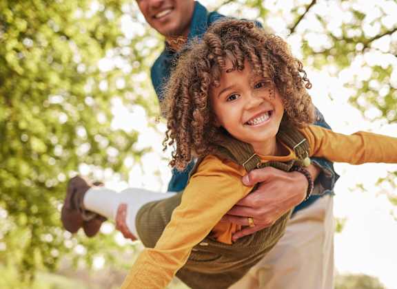 A child is being held up by an adult in a park.