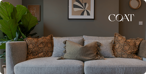 A living room with a grey couch and a large leafy plant.