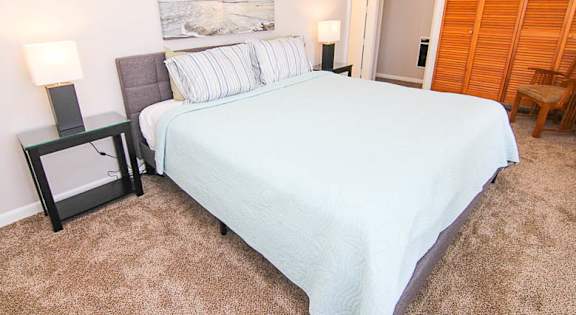 A bed with a white comforter and a painting on the wall above it.