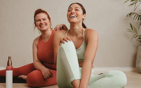 Two women are sitting on the floor, one is stretching and the other is laughing.at Station Village at Denville, Denville, NJ 07834