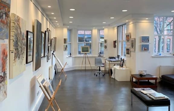 an art gallery with paintings and paintings on the wall and a table with a chair at The Trilogy Apartments, Manchester, M15 4RU