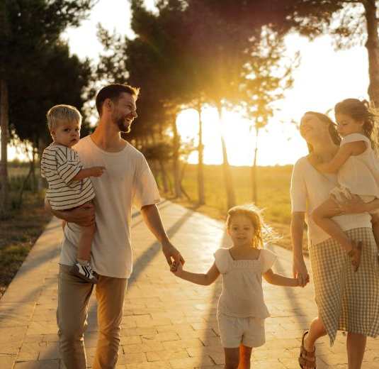 A family of four is walking hand in hand on a path.