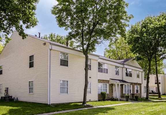 A beige two-story apartment building with a tree in front.