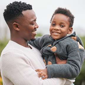 A man in a white sweater is holding a child in a grey hoodie.