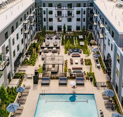 A large swimming pool is surrounded by lounge chairs and umbrellas in the middle of a courtyard.