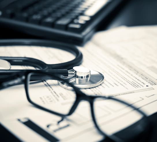 Stethoscope on top of paperwork with eye glasses and computer keyboard
