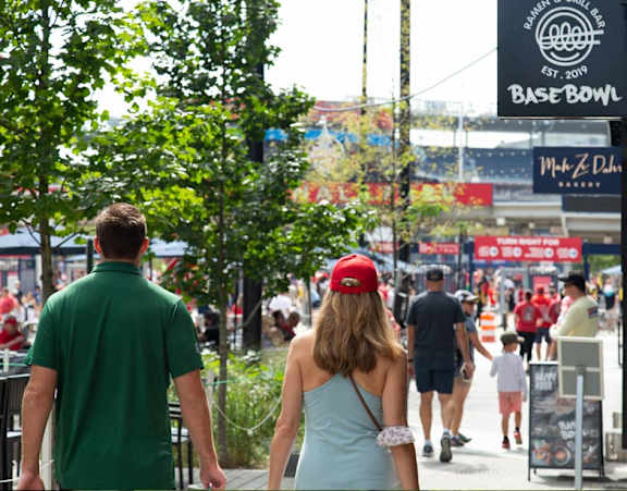 A couple walking down a street with a sign that says "Base Bowl" in the background.