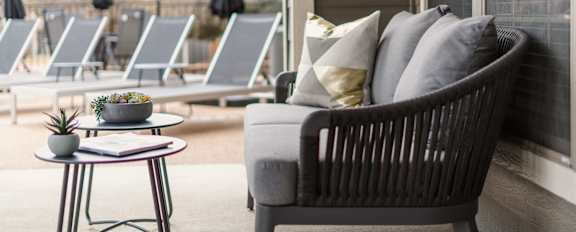 A grey wicker chair with a cushion and a small table with a plant on it.
