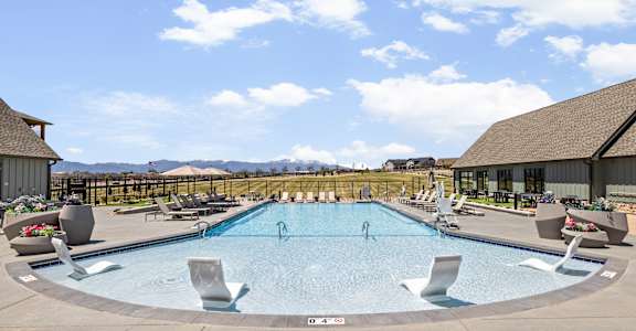 A large outdoor swimming pool surrounded by lounge chairs and a mountainous backdrop.