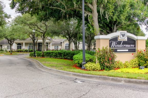 Community Entrance Sign with Decorative Plants and Trees and Leasing Office in the Background