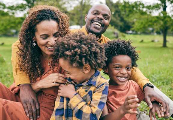 A family of four is sitting on the grass in a park.