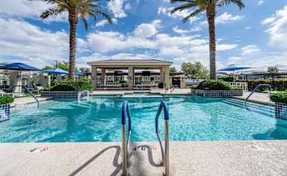 A pool surrounded by palm trees and a pavilion at Vistoria At Country Place Apartments, Tolleson, AZ, 85353