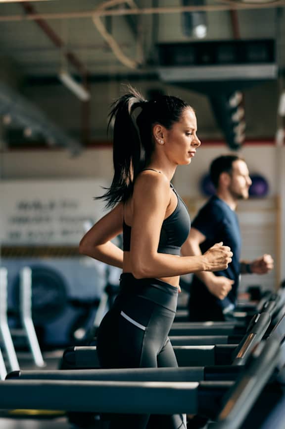 A woman is running on a treadmill in a gym.