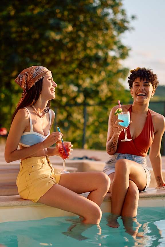Two women enjoying drinks by a pool.