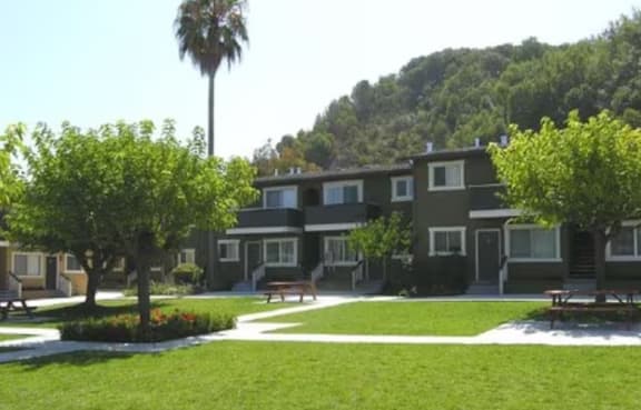 A green lawn in front of a building with trees and bushes.