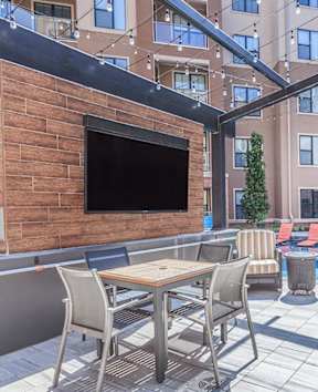 A patio with a table, chairs, and a television on a brick wall.