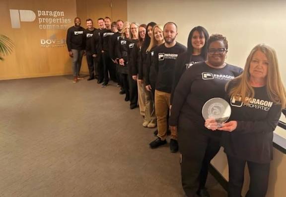 A group of people in black shirts are standing in a line, one person is holding a trophy.