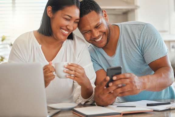 A man and woman are sitting at a table with a laptop, a cup, and a smartphone.