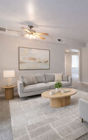 A living room with a grey couch, a wooden coffee table, and a kitchen area in the background.