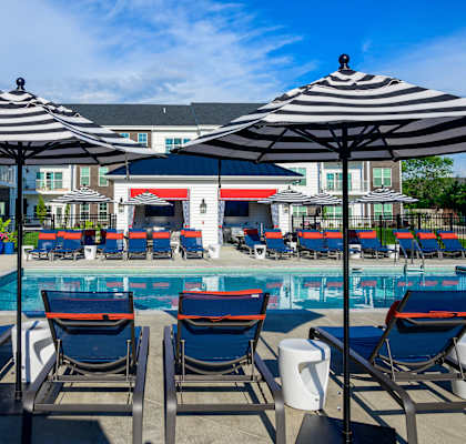 A pool area with chairs and umbrellas in front of a building.