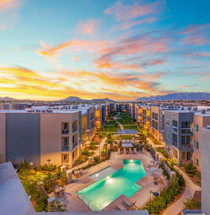 A sunset view of a pool area surrounded by apartment buildings.