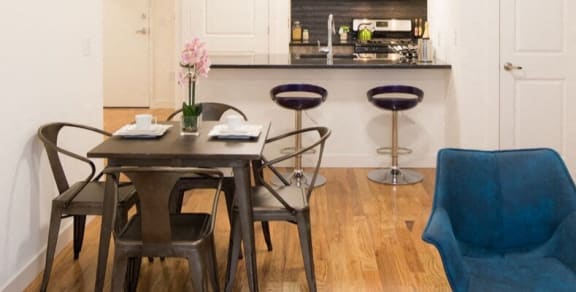 a dining room with a table and chairs and a kitchen in the background