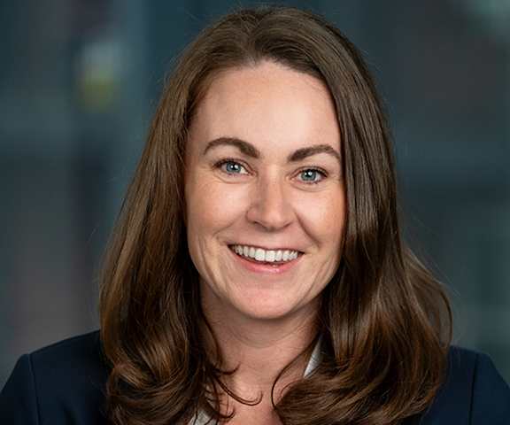 A woman with brown hair and a white shirt is smiling.