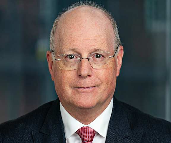 A man with glasses and a red tie is wearing a dark suit.