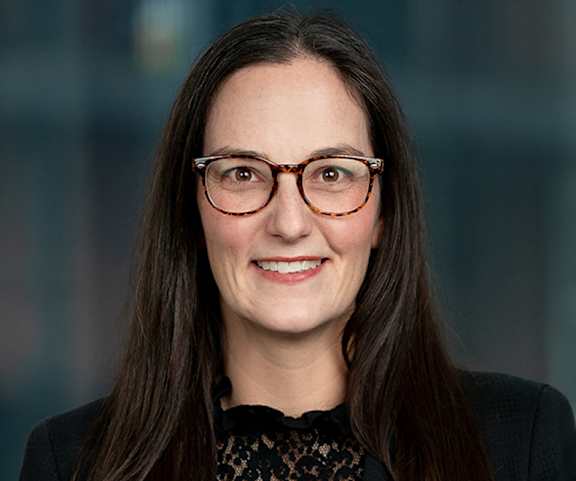 A woman with glasses and a black lace top is smiling.