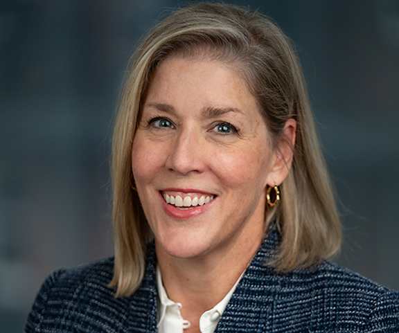 A woman with blonde hair and a white shirt is smiling.