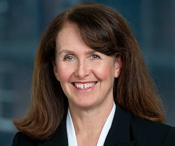 A woman with brown hair and a black blazer smiles at the camera.