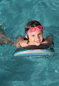 A young girl is swimming in a pool with a pink floatation device.