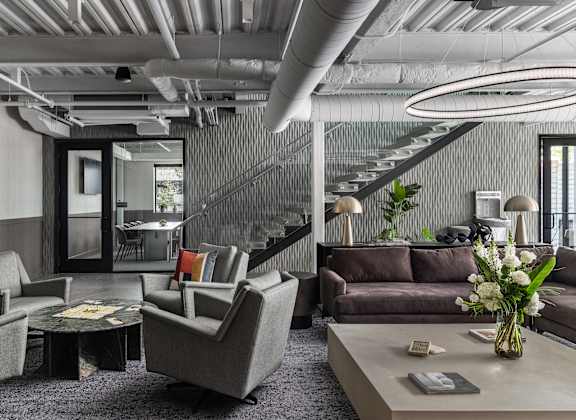 A modern living room with grey furniture and a glass staircase.