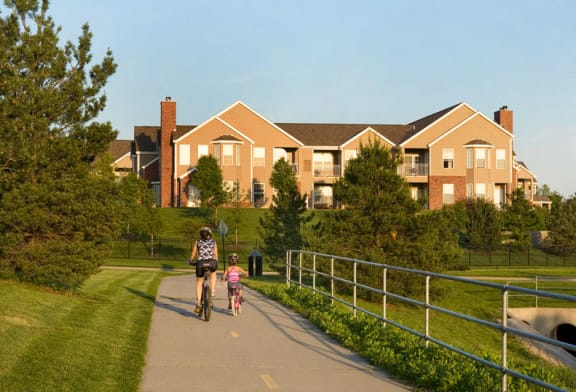 Woman and young girl riding bikes on path with landscaping along it and apartment building in background