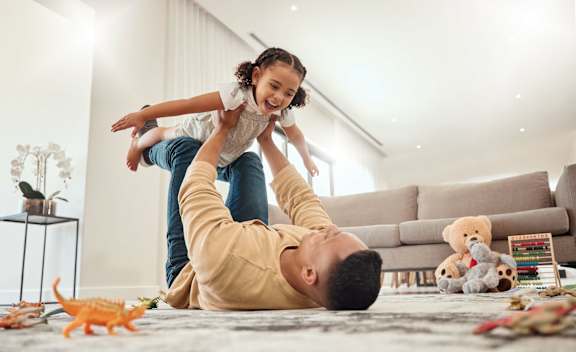 A man is lying on the floor with a child on his back at The Foundry Apartments, Bordon, GU35 9FE