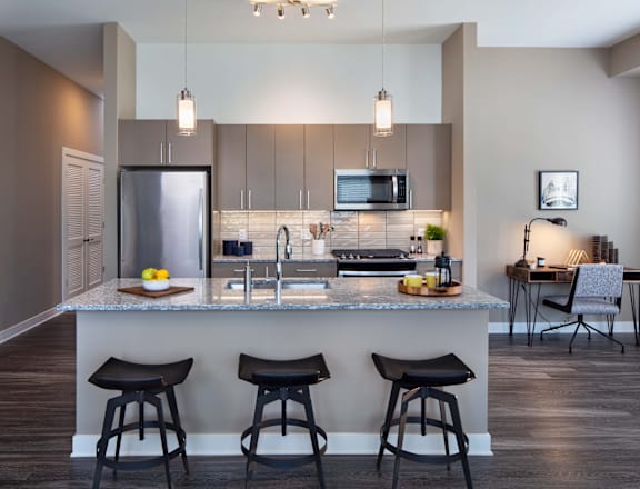 A modern kitchen with a bar area and three stools.