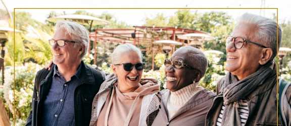 Four older adults are standing together outside.