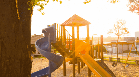 A playground with swings and a slide is bathed in sunlight at Pleasantview Apartments, Baltimore, Maryland
