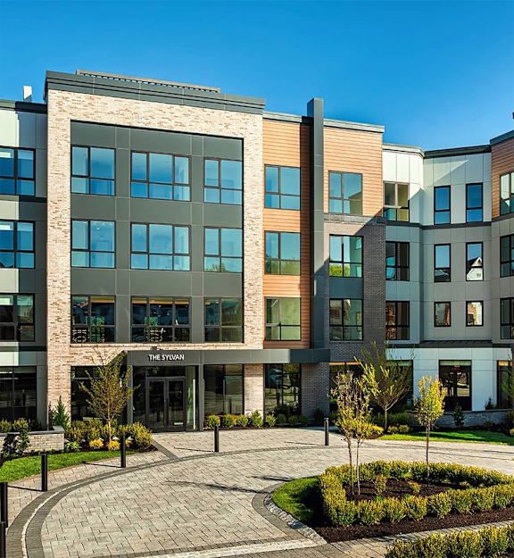 Corner view of a five-story luxury apartment building with illuminated windows at twilight.