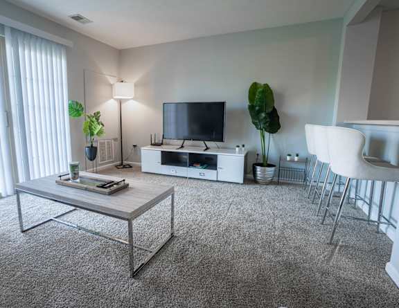 A living room with a grey carpet and a glass coffee table.