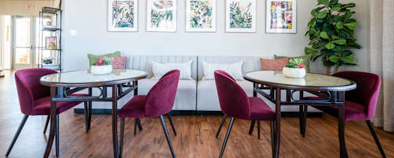A living room with a white couch, a round table with four chairs, and a potted plant.