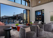 Thumbnail 11 of 52 - A modern living room with grey armchairs and a large window overlooking a cityscape at Solhavn Apartments, American Fork, Utah