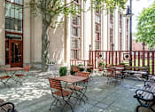 Thumbnail 14 of 23 - A patio with tables and chairs is surrounded by a building.