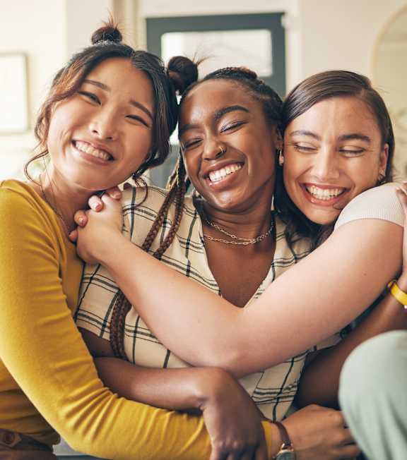 Three women hugging each other in a living room.